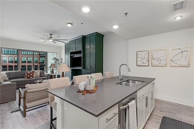 kitchen with sink, white cabinetry, green cabinetry, a center island with sink, and light wood-type flooring