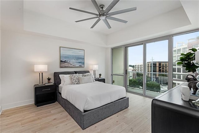 bedroom with access to outside, light hardwood / wood-style floors, a raised ceiling, and ceiling fan