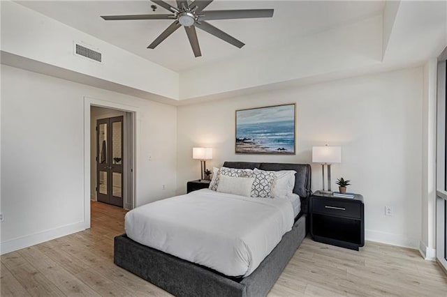 bedroom with ceiling fan, a tray ceiling, and light hardwood / wood-style flooring