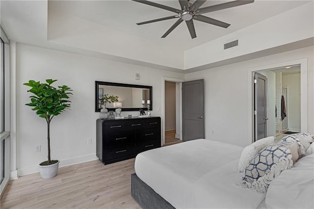 bedroom with light hardwood / wood-style flooring, a raised ceiling, and ceiling fan