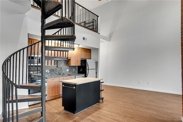 kitchen featuring a center island, tasteful backsplash, light hardwood / wood-style flooring, white refrigerator, and a towering ceiling