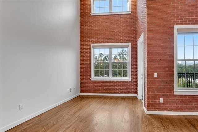 empty room with brick wall, a high ceiling, and light wood-type flooring