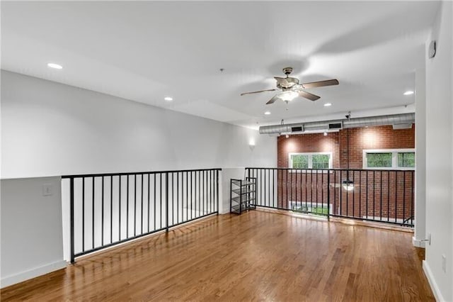 empty room with ceiling fan, hardwood / wood-style floors, and brick wall