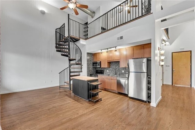 kitchen with appliances with stainless steel finishes, a towering ceiling, ceiling fan, wood-type flooring, and a center island