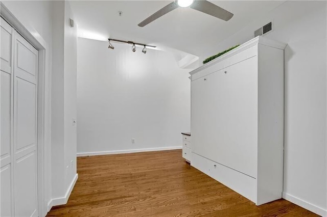 corridor with wood-type flooring and track lighting