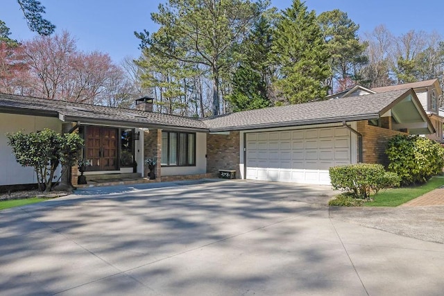 ranch-style home with driveway, an attached garage, a chimney, and brick siding