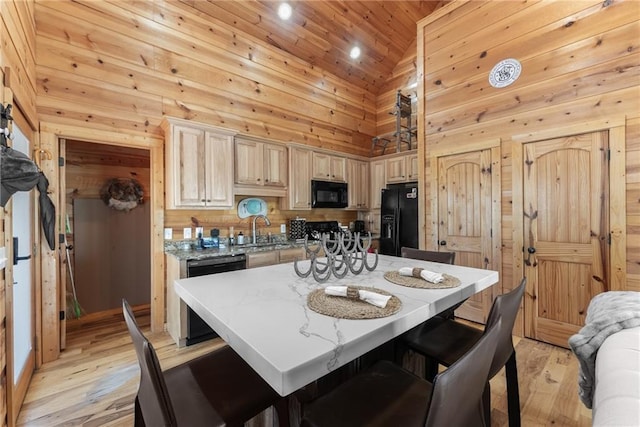 kitchen with light wood-style flooring, black appliances, a sink, high vaulted ceiling, and wooden walls