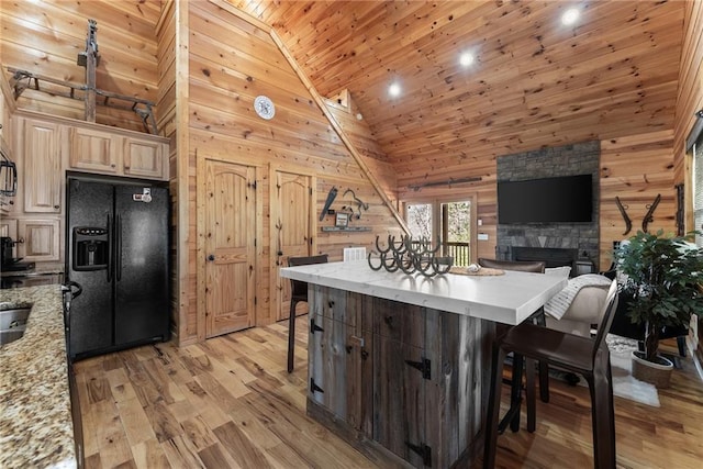 kitchen with light wood-style floors, black fridge, wooden walls, a breakfast bar area, and wood ceiling
