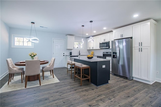 kitchen with hanging light fixtures, stainless steel appliances, a center island, and white cabinets