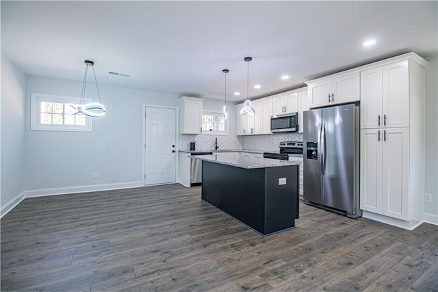 kitchen with appliances with stainless steel finishes, a center island, white cabinets, and decorative light fixtures