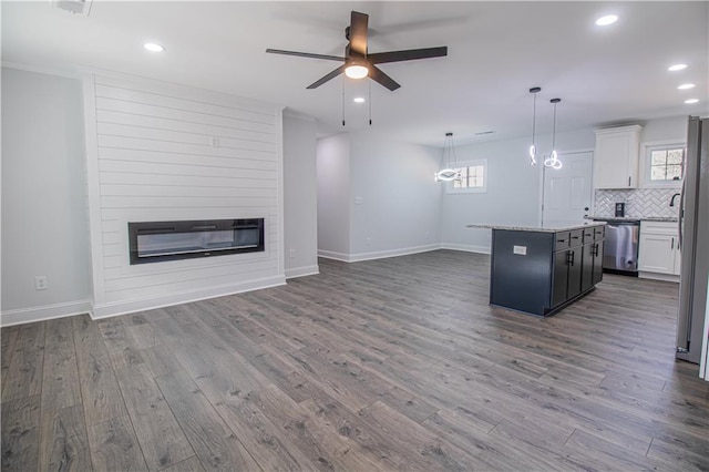 kitchen with appliances with stainless steel finishes, white cabinetry, a center island, a large fireplace, and decorative light fixtures