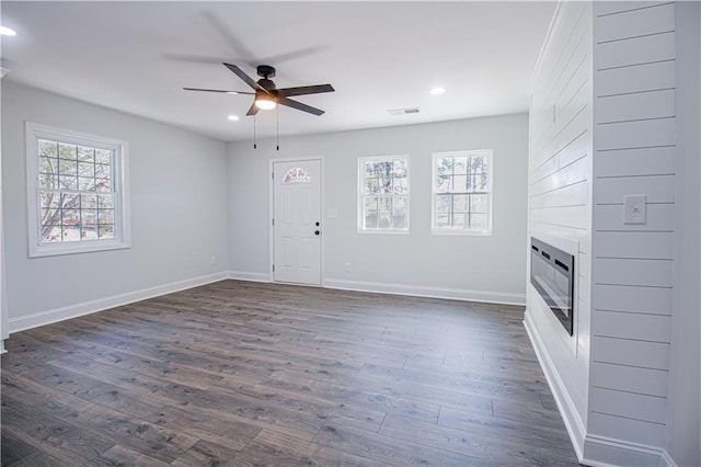 unfurnished living room featuring dark wood-type flooring, a large fireplace, and ceiling fan