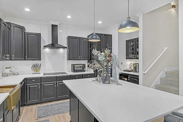 kitchen featuring wall chimney range hood, crown molding, light hardwood / wood-style floors, decorative light fixtures, and black electric stovetop