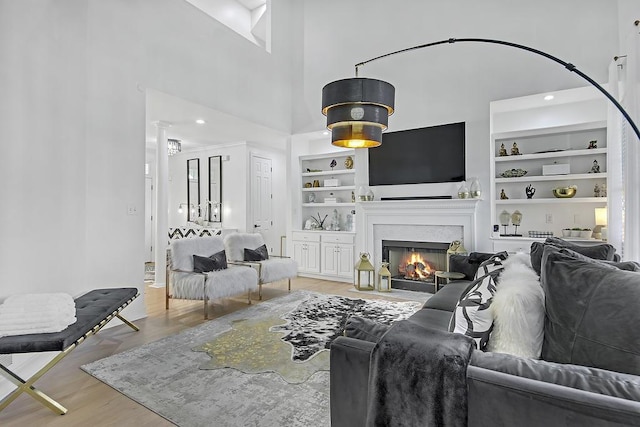 living room featuring built in shelves, light wood-type flooring, and a high ceiling