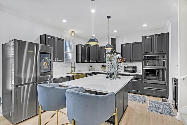 kitchen featuring appliances with stainless steel finishes, sink, light hardwood / wood-style floors, a kitchen island, and hanging light fixtures