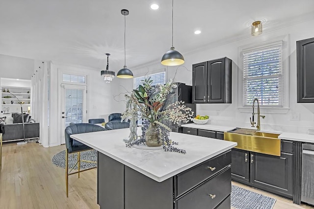 kitchen with light wood-type flooring, ornamental molding, sink, decorative light fixtures, and a center island