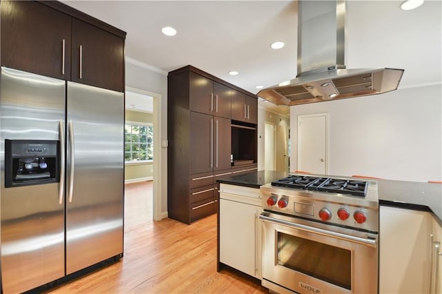 kitchen with light wood finished floors, stainless steel appliances, dark countertops, ornamental molding, and ventilation hood