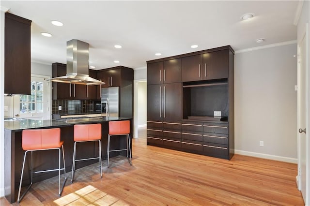 kitchen with island range hood, appliances with stainless steel finishes, a peninsula, dark brown cabinets, and crown molding