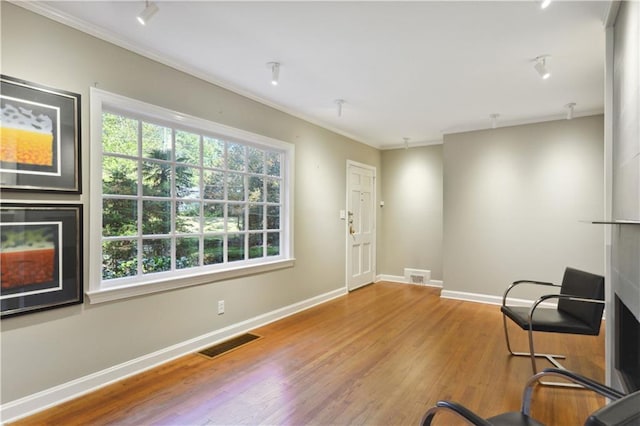 sitting room with baseboards, visible vents, wood finished floors, and ornamental molding