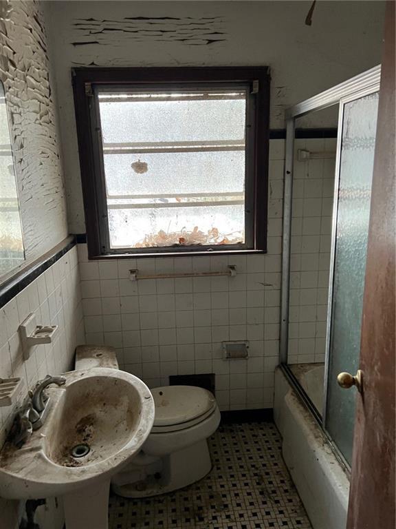 full bathroom with sink, tile patterned flooring, toilet, enclosed tub / shower combo, and tile walls