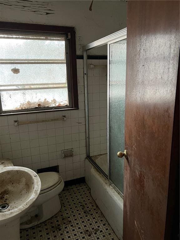 bathroom with tile patterned flooring, toilet, bath / shower combo with glass door, and tile walls