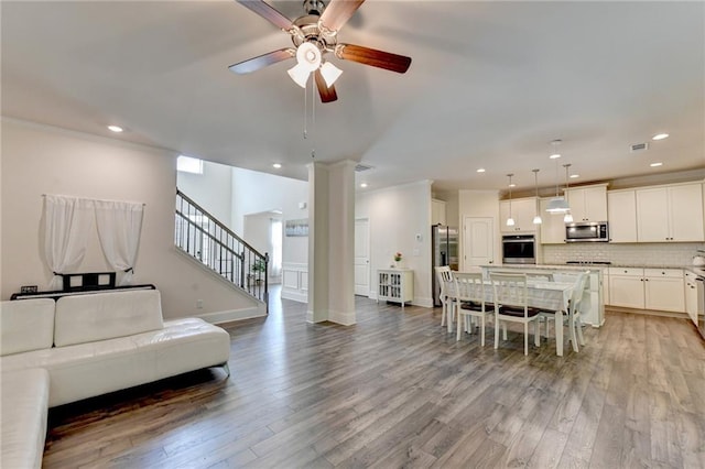 living room featuring decorative columns, light hardwood / wood-style floors, ornamental molding, and ceiling fan