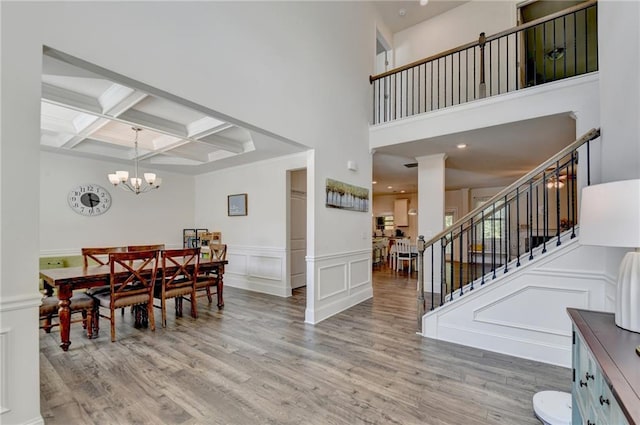 dining room featuring coffered ceiling, beamed ceiling, light hardwood / wood-style floors, and a high ceiling