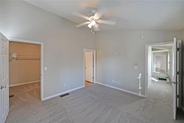 unfurnished bedroom featuring light colored carpet, lofted ceiling, visible vents, and a spacious closet