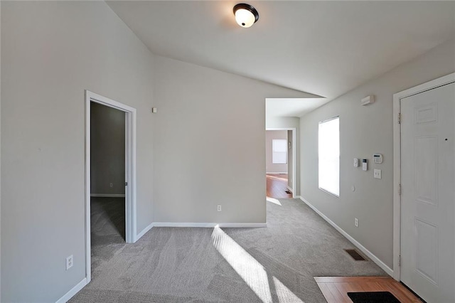 spare room featuring light carpet, baseboards, visible vents, and vaulted ceiling