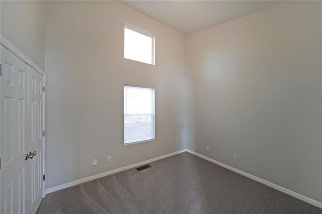 unfurnished room with a high ceiling, a healthy amount of sunlight, visible vents, and baseboards