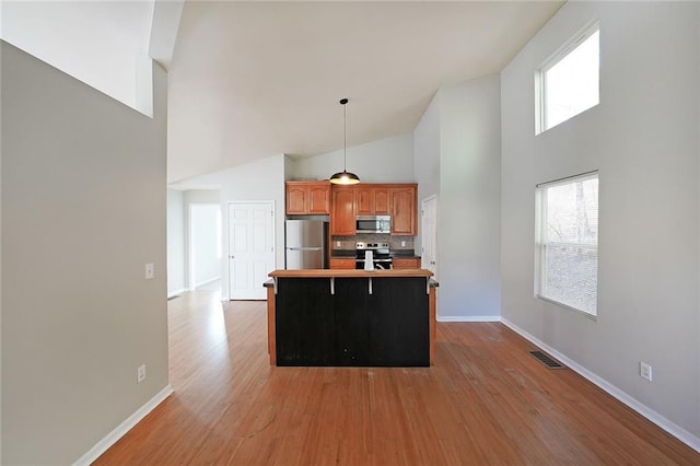 kitchen with light wood-style flooring, stainless steel appliances, visible vents, hanging light fixtures, and brown cabinets