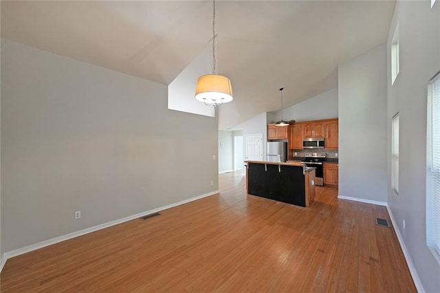 kitchen with stainless steel appliances, a kitchen island, open floor plan, a kitchen bar, and decorative light fixtures