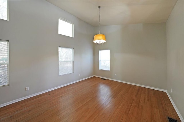 unfurnished room with a towering ceiling, hardwood / wood-style flooring, baseboards, and visible vents