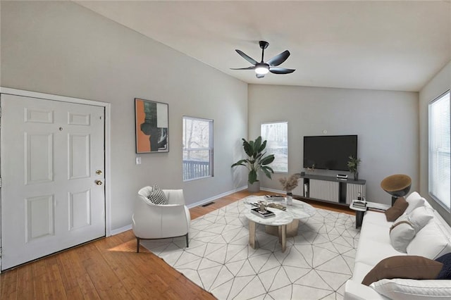 living room with lofted ceiling, a ceiling fan, visible vents, baseboards, and light wood finished floors