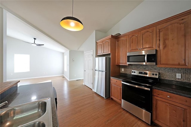 kitchen with appliances with stainless steel finishes, brown cabinetry, vaulted ceiling, and a sink