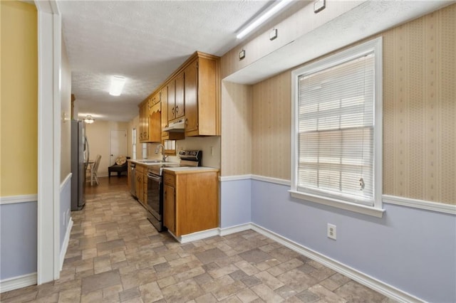 136 Pine St, Covington, GA 30014 - kitchen with appliances with stainless steel finishes, under cabinet range hood, light countertops, stone finish floors, and brown cabinets
