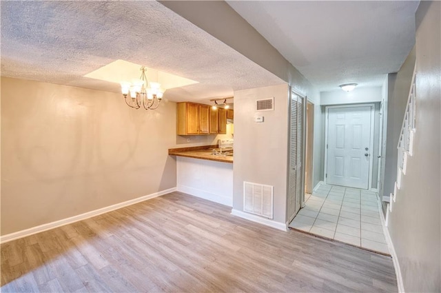 interior space featuring pendant lighting, a notable chandelier, a textured ceiling, kitchen peninsula, and light wood-type flooring