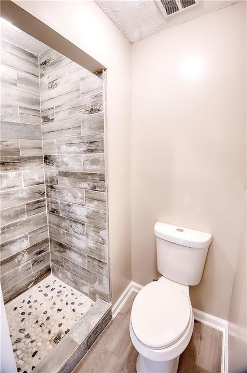 bathroom with a tile shower, wood-type flooring, and toilet