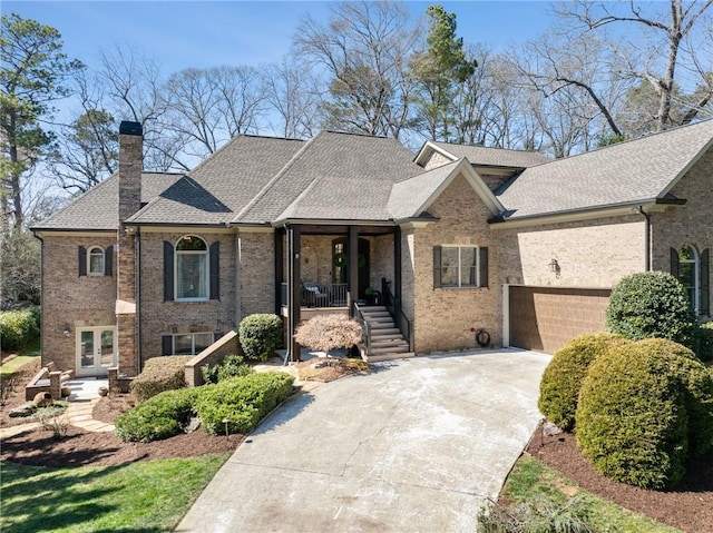 view of front of home featuring brick siding, concrete driveway, french doors, roof with shingles, and a chimney