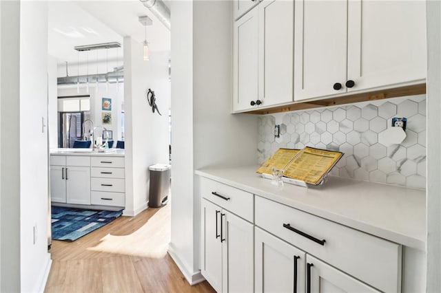 bar with white cabinetry, decorative backsplash, sink, light hardwood / wood-style flooring, and pendant lighting