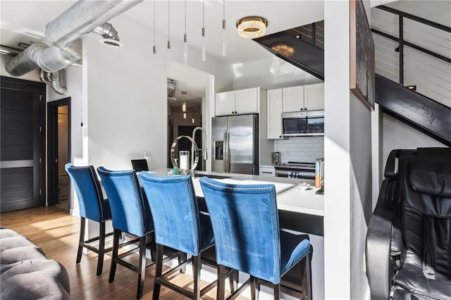 kitchen with white cabinets, decorative backsplash, light hardwood / wood-style floors, and stainless steel appliances