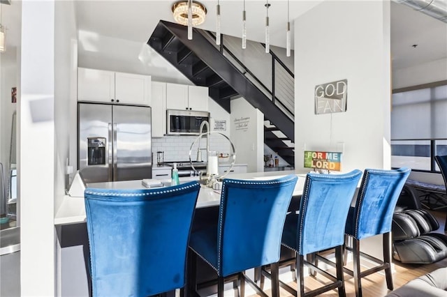 kitchen featuring hanging light fixtures, white cabinets, tasteful backsplash, a kitchen bar, and stainless steel appliances