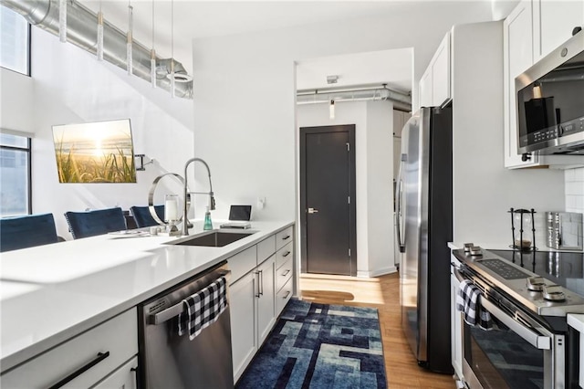kitchen with pendant lighting, sink, white cabinets, light wood-type flooring, and stainless steel appliances