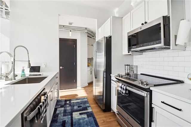 kitchen with appliances with stainless steel finishes, white cabinetry, sink, backsplash, and light wood-type flooring