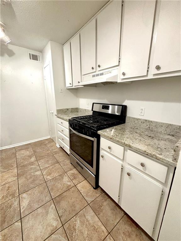 kitchen featuring gas stove, a textured ceiling, white cabinets, under cabinet range hood, and visible vents