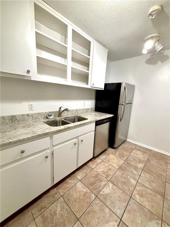 kitchen with light tile patterned floors, white cabinetry, a textured ceiling, stainless steel appliances, and a sink