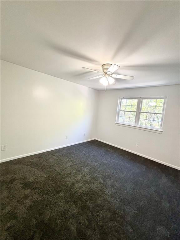 empty room with ceiling fan, dark colored carpet, and baseboards