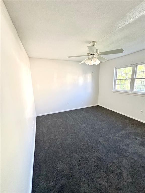 spare room featuring dark carpet, baseboards, a ceiling fan, and a textured ceiling
