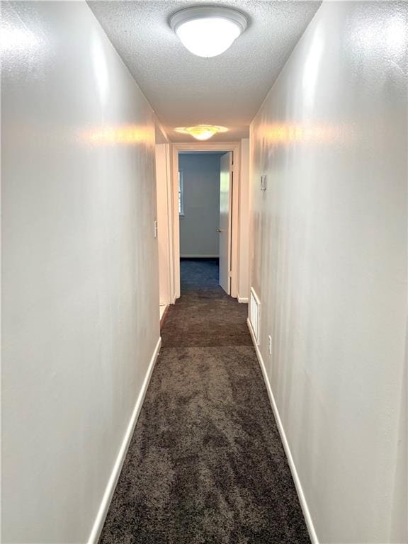 corridor with visible vents, baseboards, dark colored carpet, and a textured ceiling