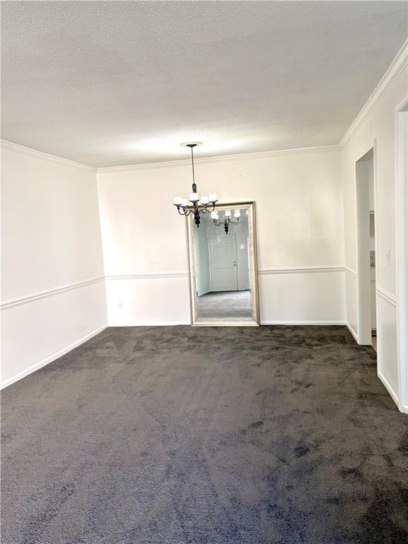 carpeted spare room featuring crown molding, baseboards, and a notable chandelier